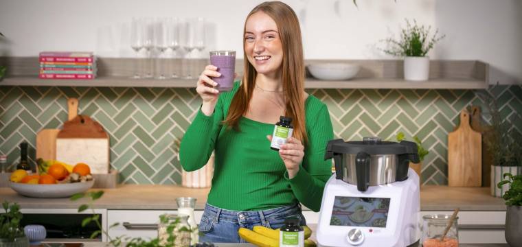 Junge Frau in einer Küche mit Monsieur Cuisine, in einer Hand ein Blaubeer-Shake Junge Frau in einer Küche mit Monsieur Cuisine, in einer Hand ein Blaubeer-Shake