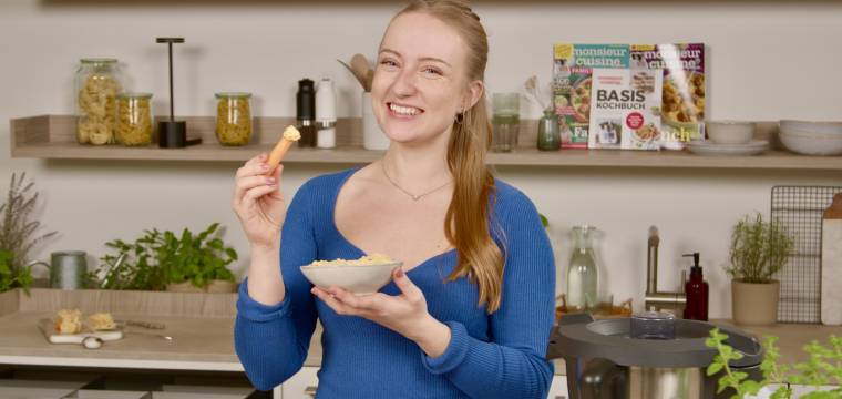 Junge Frau in einer Küche mit einer Schale und einem Snack in der Hand