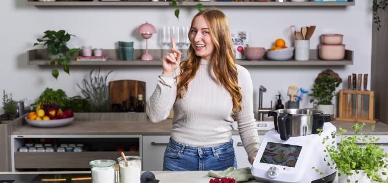 Frau in einer Küche mit Monsieur Cuisine, hebt den Finger wissend