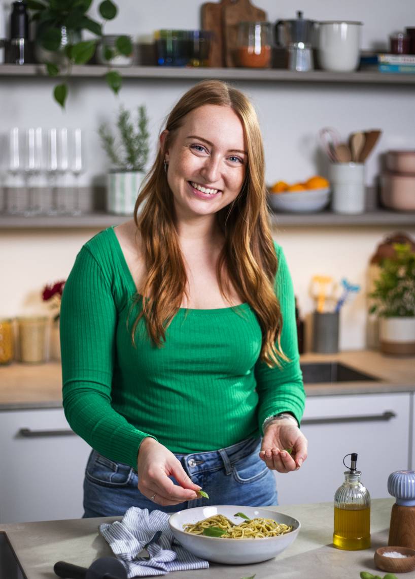Junge Frau mit langen Haaren und grünem Pullover steht mit Monsieur Cuisine in der Küche Junge Frau mit langen Haaren und grünem Pullover steht mit Monsieur Cuisine in der Küche