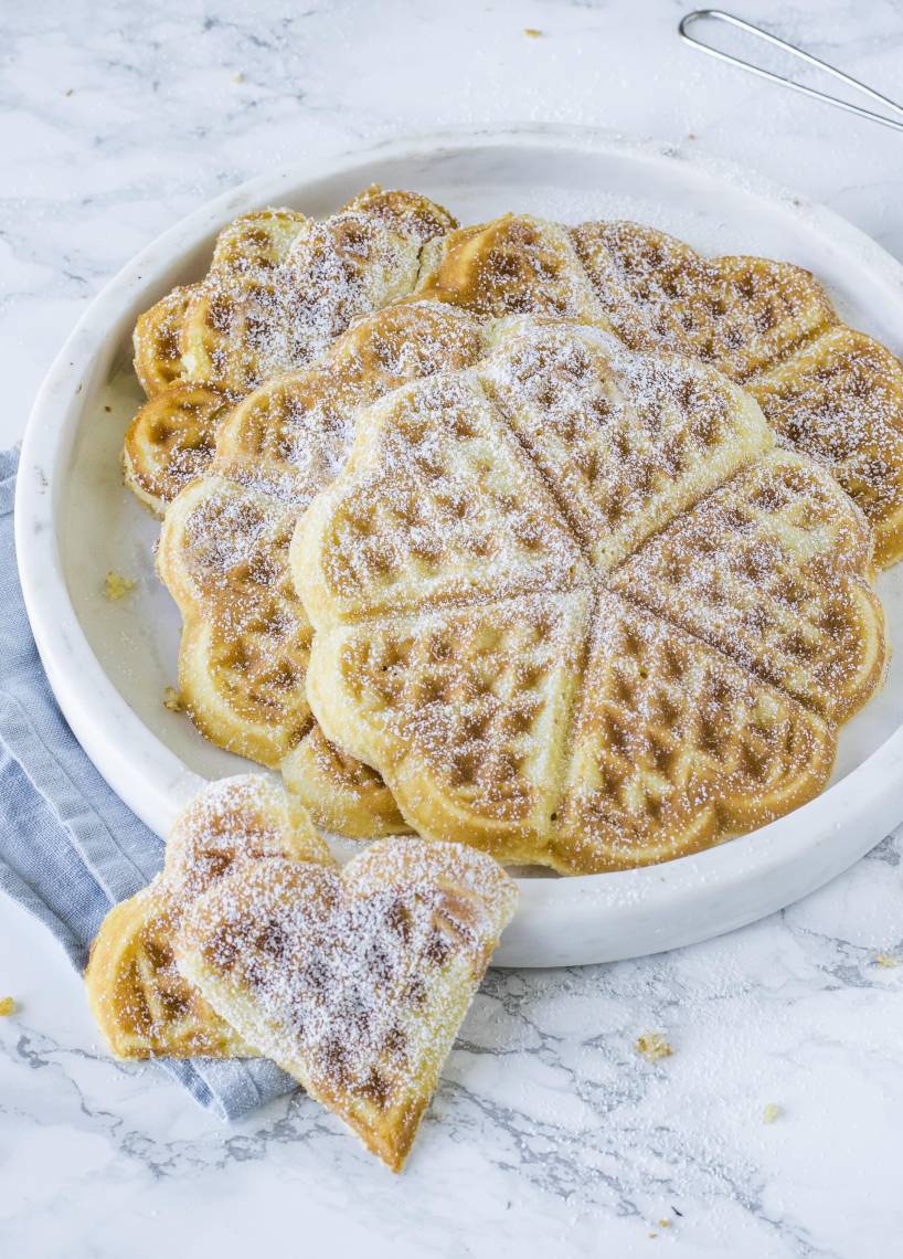 Waffeln in Herzformen auf einem Teller mit Puderzucker überstreut