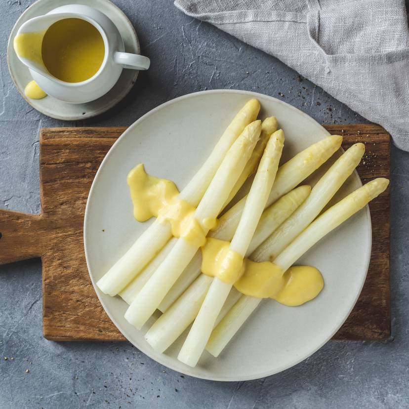 Weiße Spargelstangen mit Sauce hollandaise auf rundem weißen Teller