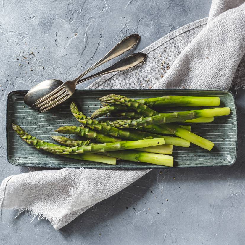Grüner Spargel auf einem schmalen Teller mit Löffeln.