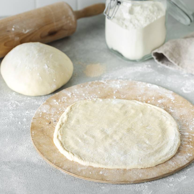 Ausgerollter Pizzateig auf einem Holzbrett.