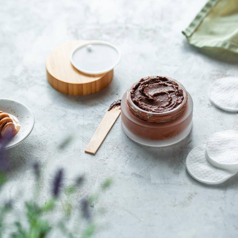 Braune Maske in Glasgefäß mit Holztiegel, Wattepads und Honig