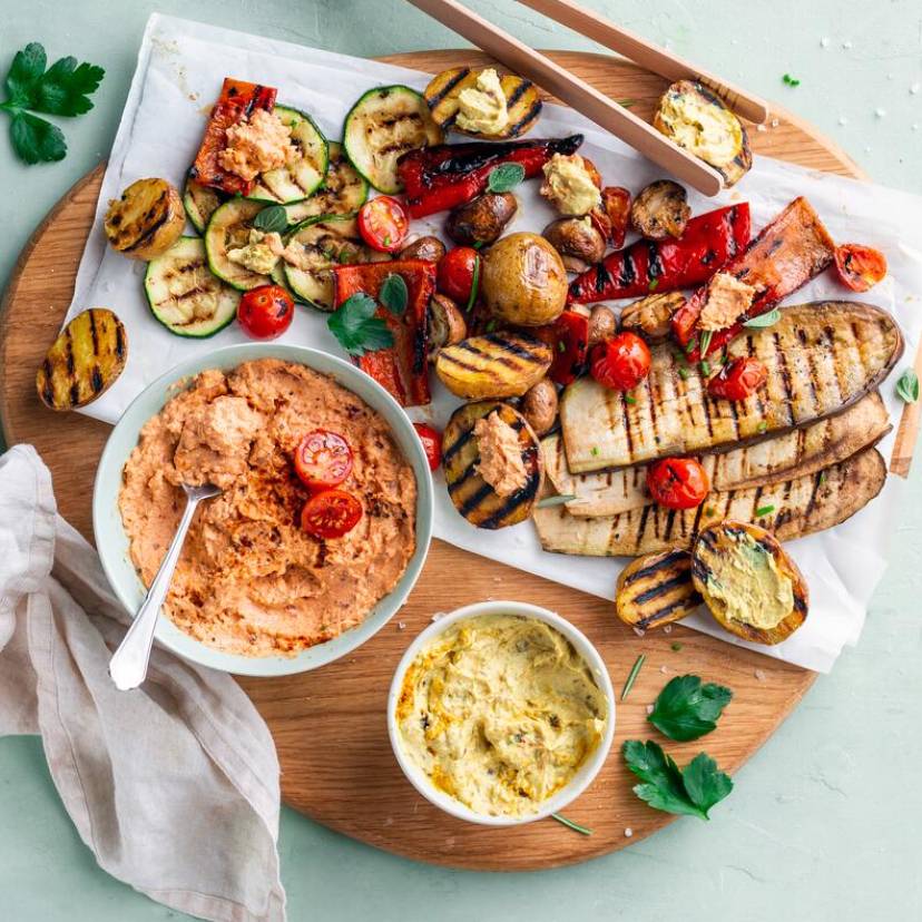 Grillgemüse und Dips auf rundem Holzbrett mit Grillzange aus Holz
