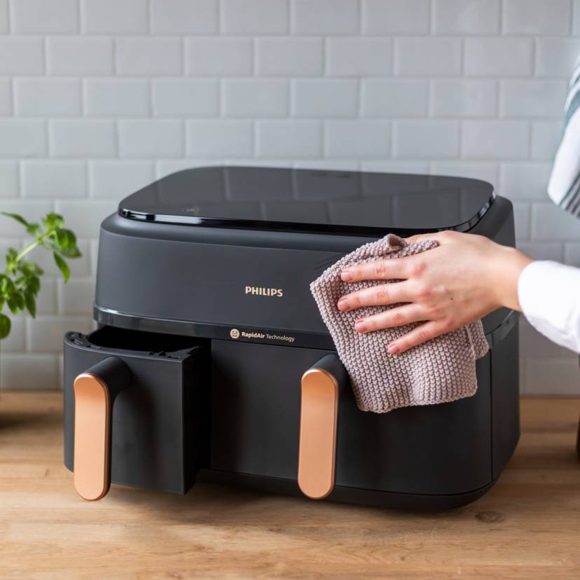 Eine Hand hält einen Lappen und wischt die Heißluftfritteuse ab