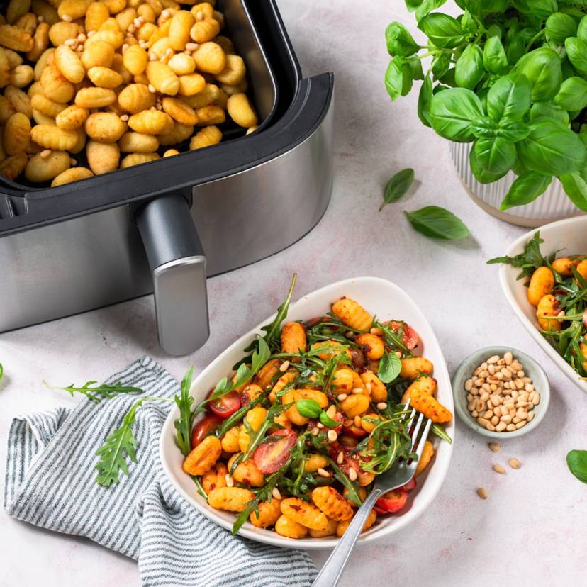 Gnocchi mit Ruccola und Tomaten auf weißen Tellern, daneben der Airfryer mit Gnocchi in der Schublade
