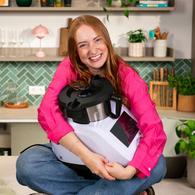 Eine Frau sitzt auf der Arbeitsplatte ihrer Küche und hält den Monsieur Cuisine im Arm