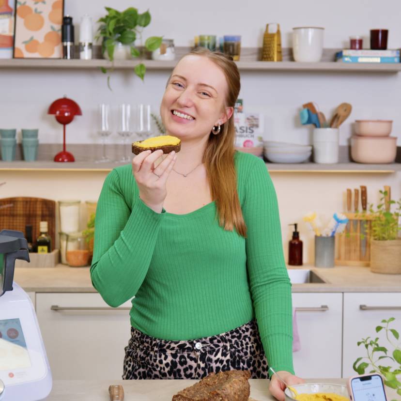 Junge Frau in einer Küche mit Monsieur Cuisine, hält eine Scheibe Brot in der Hand und freut sich