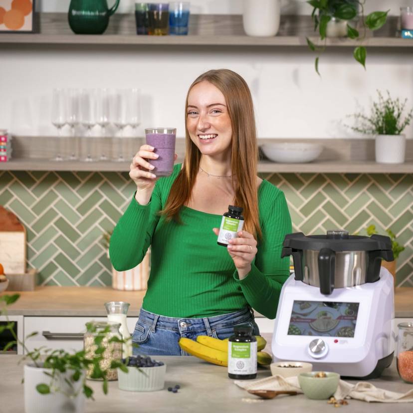Junge Frau in einer Küche mit Monsieur Cuisine, in einer Hand ein Blaubeer-Shake