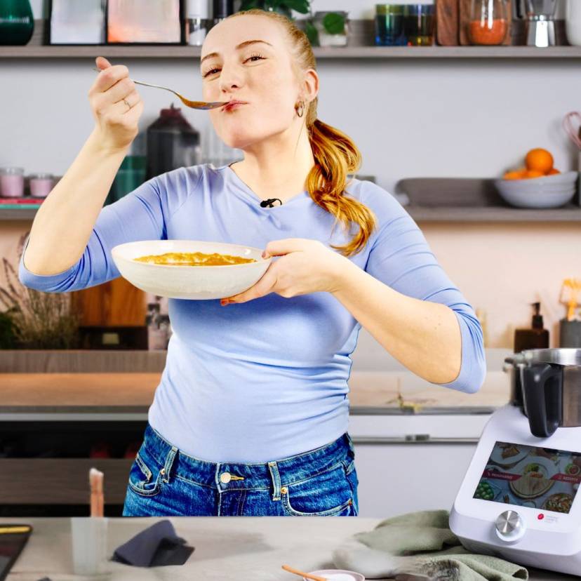 Junge Frau in einer Küche mit einem Teller Tomatensuppe, neben dem Monsieur Cuisine