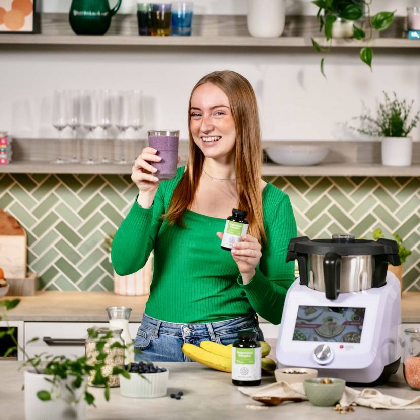 Junge Frau mit einem Blaubeershake in einer Küche neben dem Monsieur Cuisine