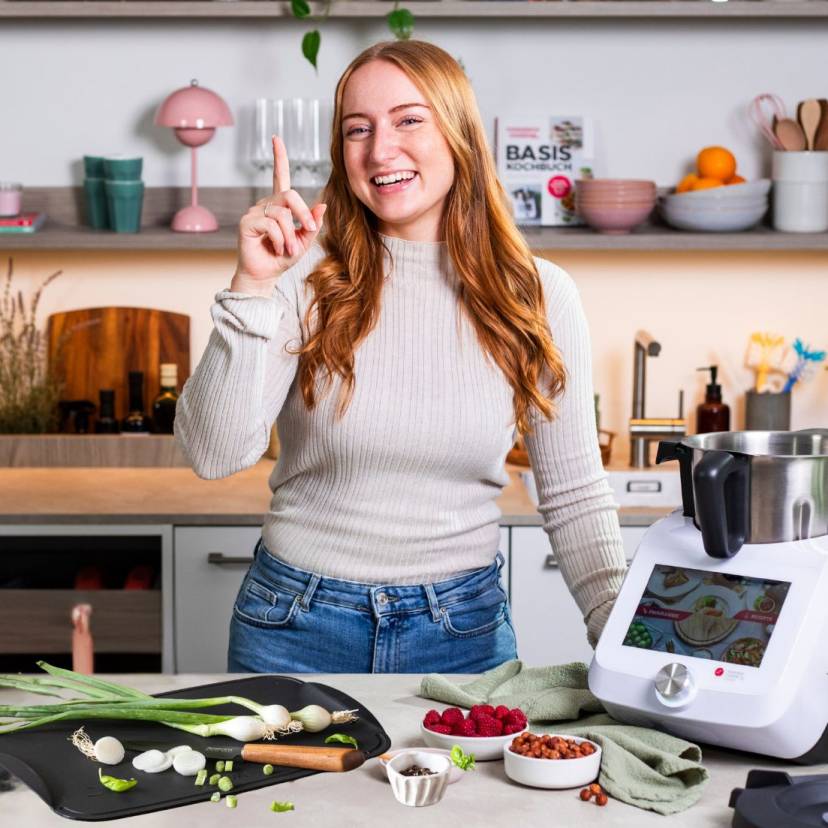 Junge Frau in einer Küche mit dem Monsieur Cuisine und einem Schneidebrett