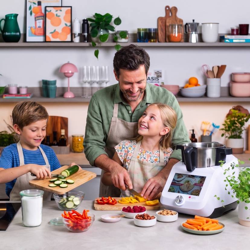Ein Mann und zwei Kinder in einer Küche mit Monsieur Cuisine beim Gemüse schneiden