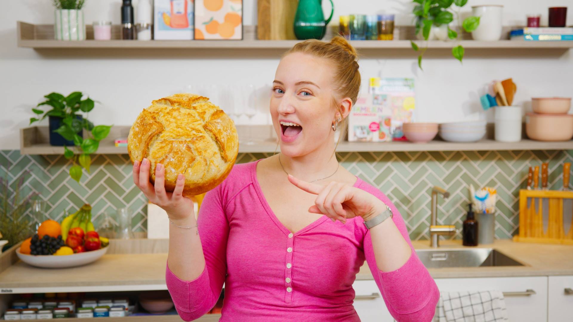 Isy hält selbstgebackenes Brot in der Hand und mit der ynderen Hand zeigt sie drauf